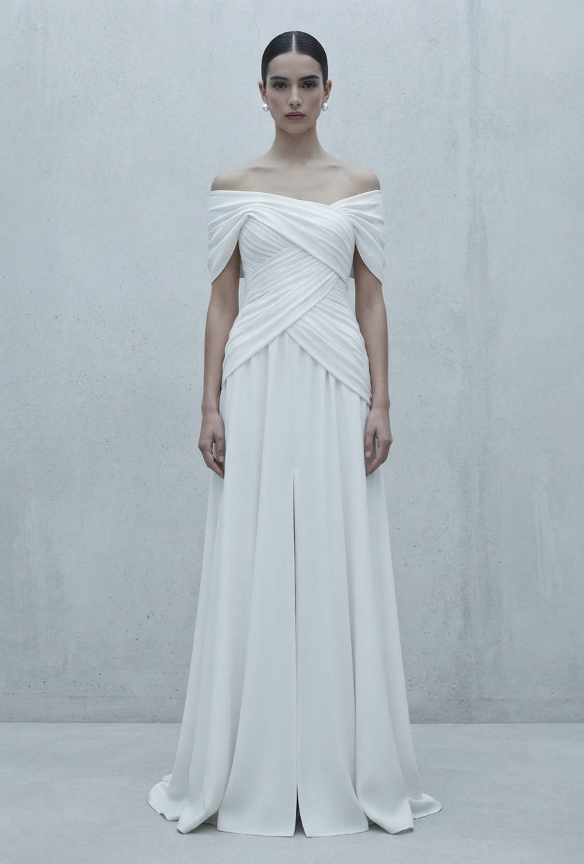 Vestido de novia de inspiración helénica con escote cruzado tipo hombros caídos y abertura frontal en la falda de la Colección Mara.