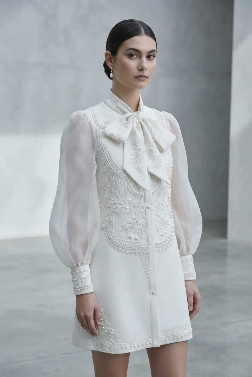 Vestido corto de novia de manga larga abullonada de gasa transparente, cuello alto con lazada y detalles de bordados de pedrería de la Colección Alma - Boda Civil.